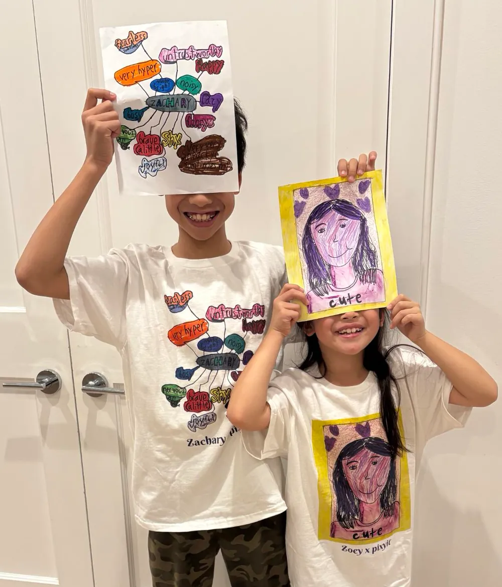 Two young creators holding up their drawings, each wearing a T-shirt printed with the same drawing.